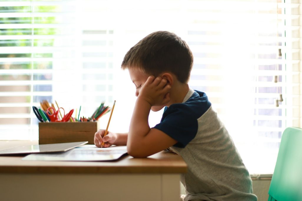 Un garçon assis à un bureau, concentré sur le dessin, crayons colorés à proximité.