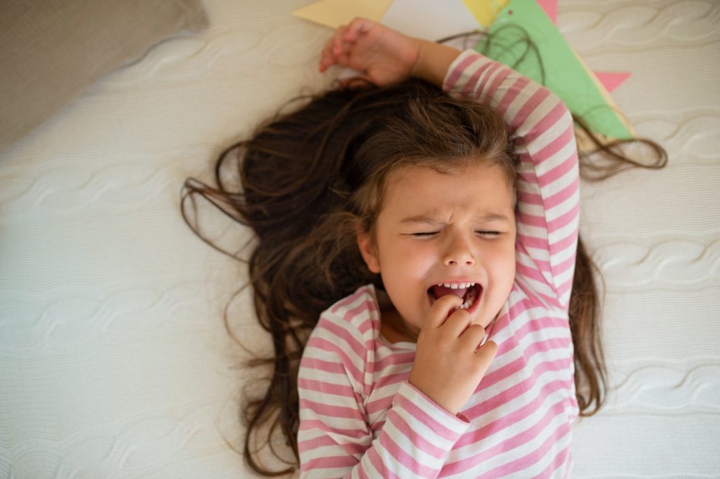 Une petite fille avec de longs cheveux bruns, en train de pleurer sur un lit.